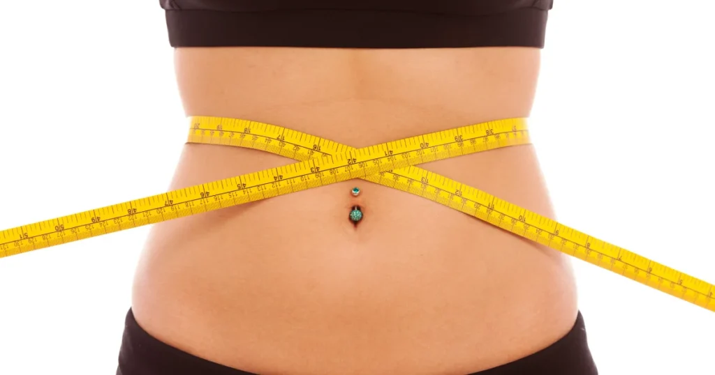 Close-up of a woman's waist being measured with a yellow tape measure to track weight loss progress.